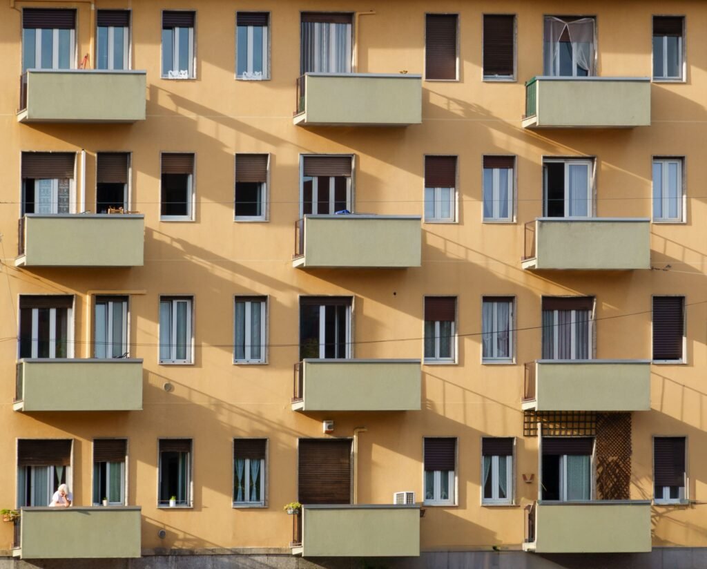 Facade of an apartment building with multiple balconies and windows in sunlight.