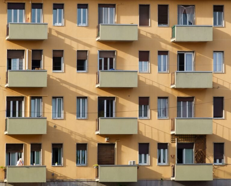 Facade of an apartment building with multiple balconies and windows in sunlight.